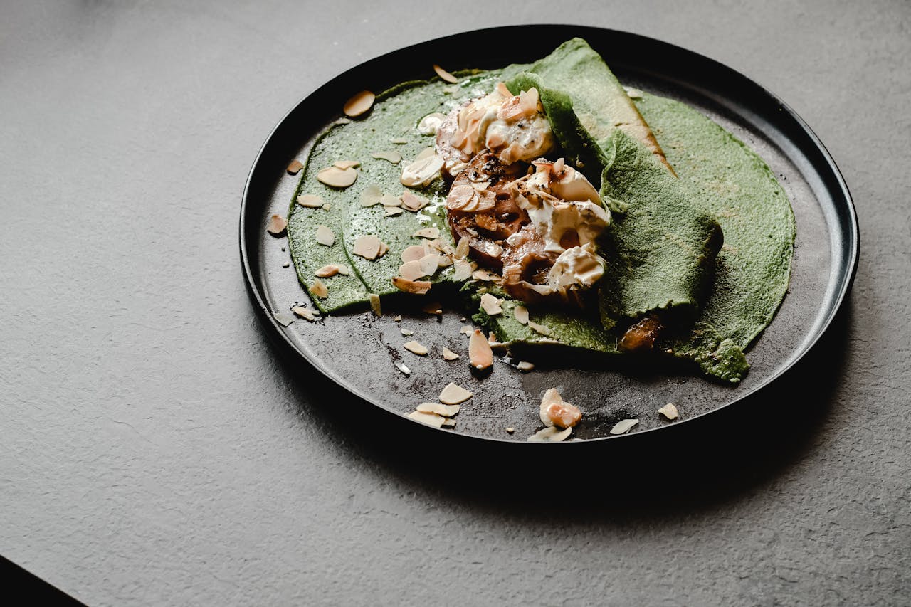 Delicious green crêpes served with almonds and cream on a black plate.